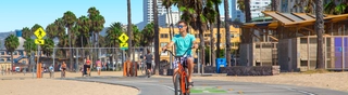 Man wearing blue shirt on red bike going down the road while thier are buildings and trees in the background