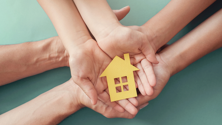 Adult and child hands holding paper house