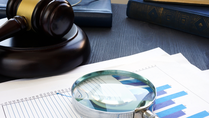 Gavel and Magnifying glass with business documents.